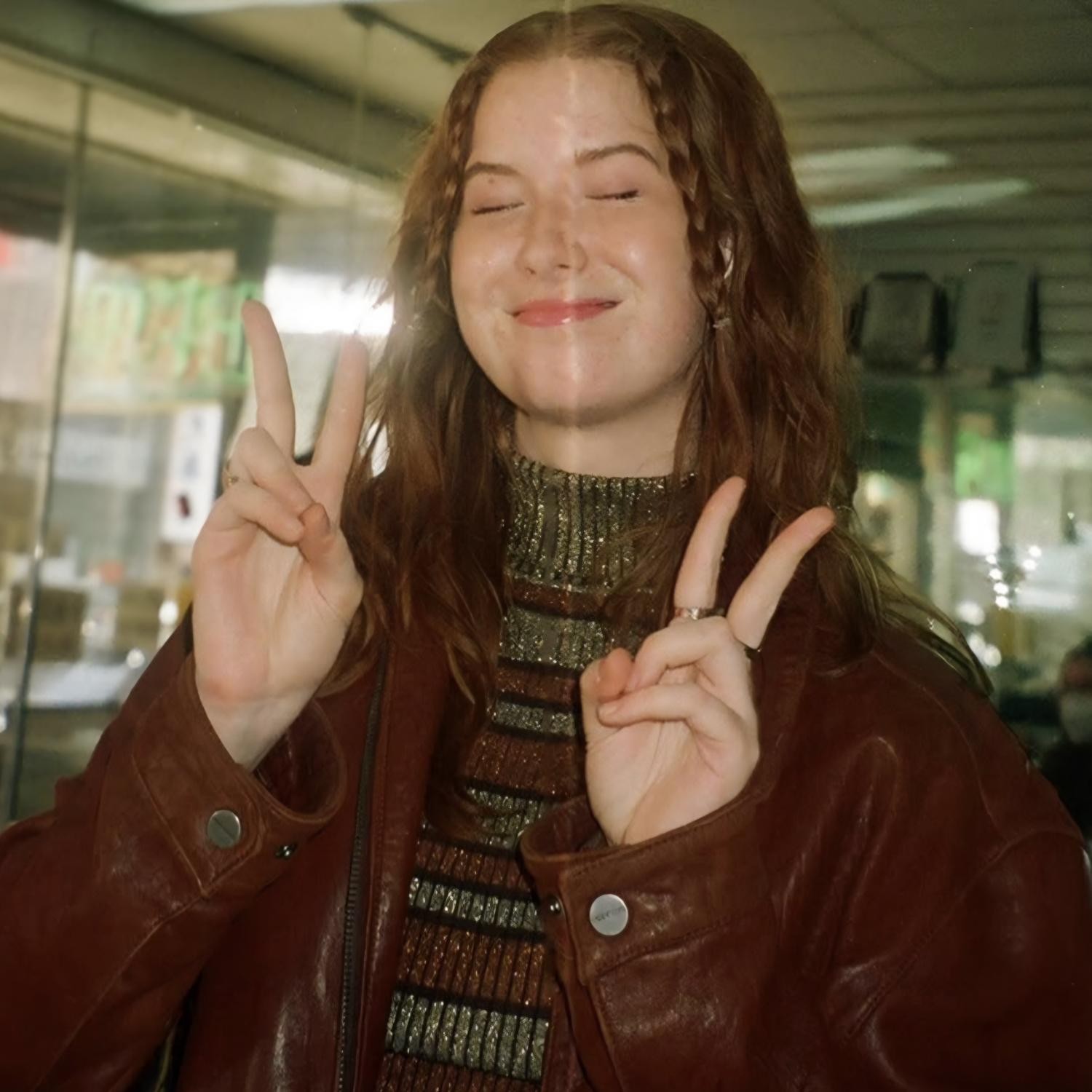 Kate Broderick in a leather jacket, smiling with both hands up.
